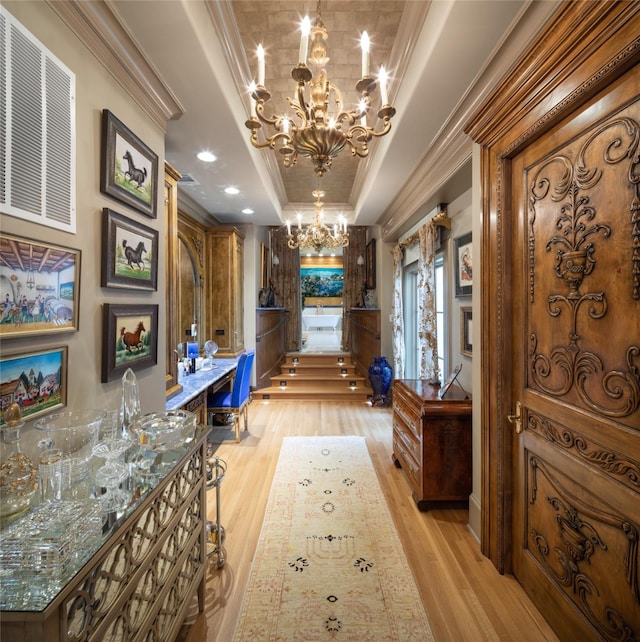 corridor featuring a tray ceiling, light hardwood / wood-style flooring, a notable chandelier, and crown molding