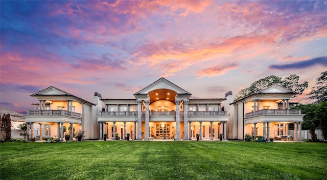 back house at dusk with a lawn and a balcony