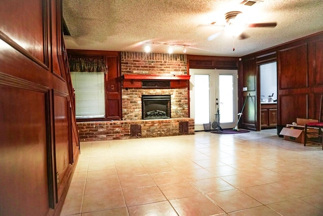 tiled living room with french doors, ceiling fan, a fireplace, a textured ceiling, and brick wall