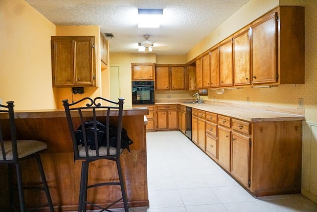 kitchen featuring ceiling fan, sink, a textured ceiling, a breakfast bar area, and black appliances