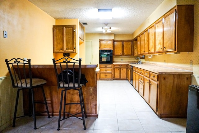 kitchen featuring a kitchen bar, ceiling fan, black appliances, and a textured ceiling