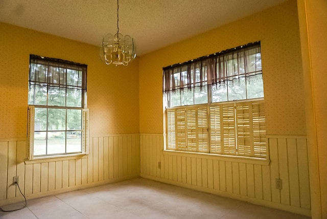 empty room featuring a chandelier, a textured ceiling, and plenty of natural light