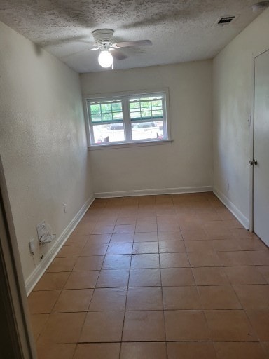 empty room with ceiling fan, light tile patterned flooring, and a textured ceiling