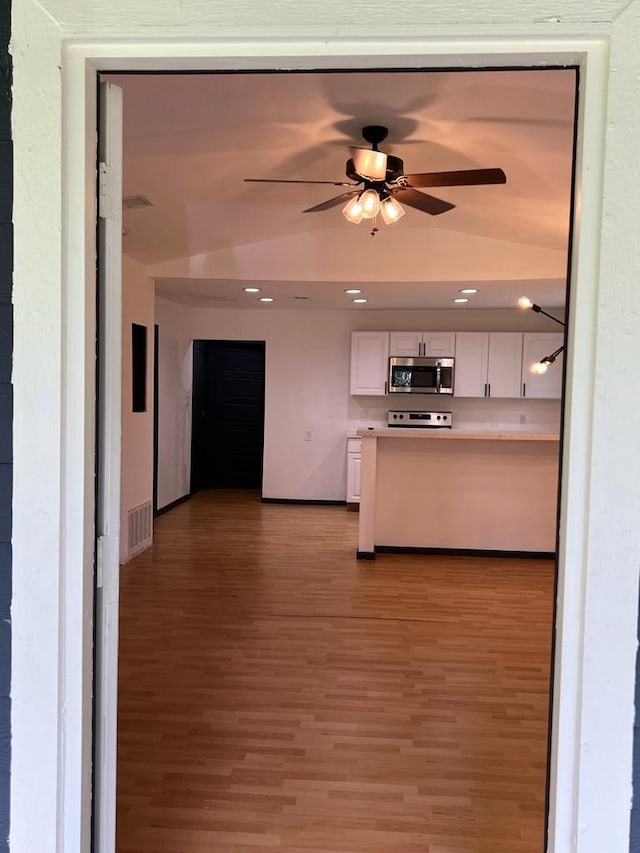 kitchen featuring vaulted ceiling, stainless steel appliances, white cabinetry, and hardwood / wood-style flooring