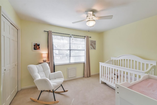 bedroom featuring a nursery area, light carpet, ceiling fan, and a closet