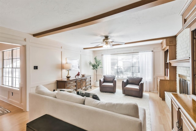 living room featuring beamed ceiling, plenty of natural light, light wood-type flooring, and a brick fireplace