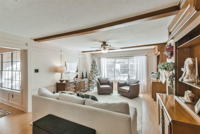 living room featuring beamed ceiling, a textured ceiling, light hardwood / wood-style floors, and ceiling fan