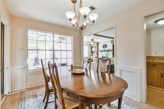 dining area with ceiling fan with notable chandelier, sink, and light wood-type flooring