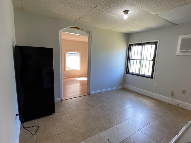 spare room with plenty of natural light, a drop ceiling, and light tile patterned floors