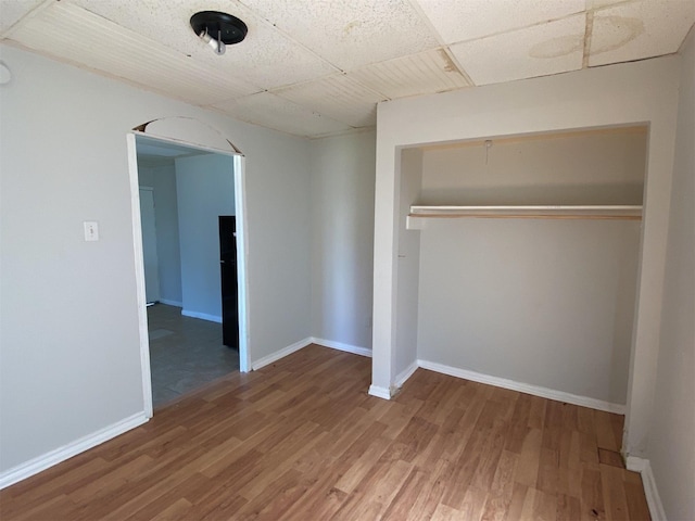 unfurnished bedroom with a closet, hardwood / wood-style floors, and a drop ceiling