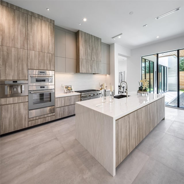 kitchen with sink, a center island with sink, appliances with stainless steel finishes, and light brown cabinets