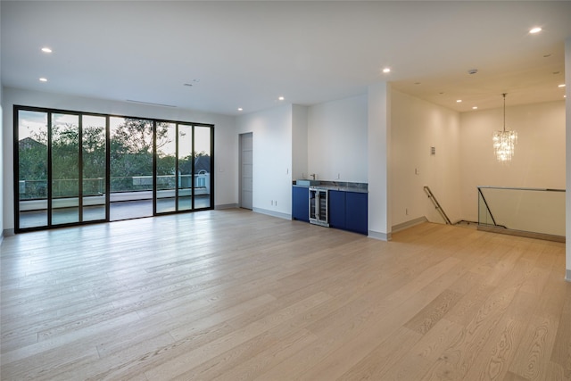 unfurnished living room featuring a chandelier, beverage cooler, and light hardwood / wood-style flooring