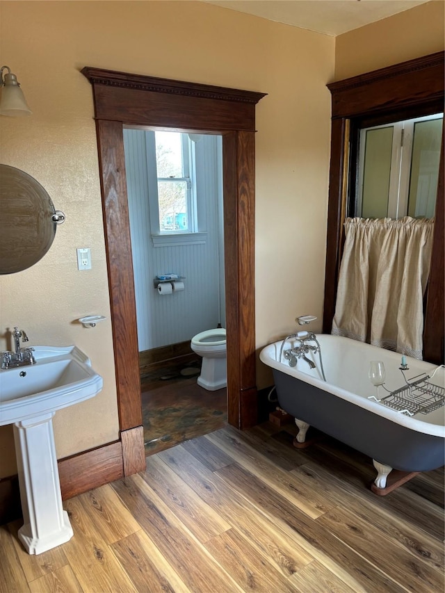 bathroom with a tub to relax in, hardwood / wood-style flooring, toilet, and sink