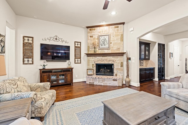 living room featuring ceiling fan, a stone fireplace, and dark hardwood / wood-style flooring