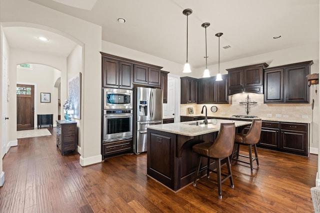 kitchen with dark hardwood / wood-style flooring, a center island with sink, decorative light fixtures, and appliances with stainless steel finishes