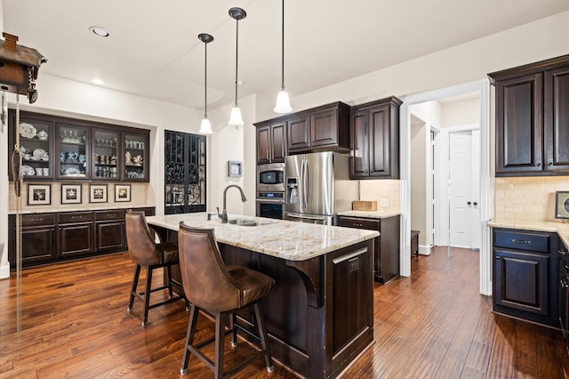 kitchen featuring dark brown cabinetry, dark wood-type flooring, an island with sink, and stainless steel appliances