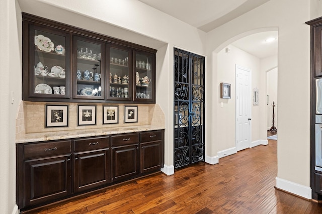 bar featuring dark brown cabinets, light stone countertops, dark wood-type flooring, and tasteful backsplash