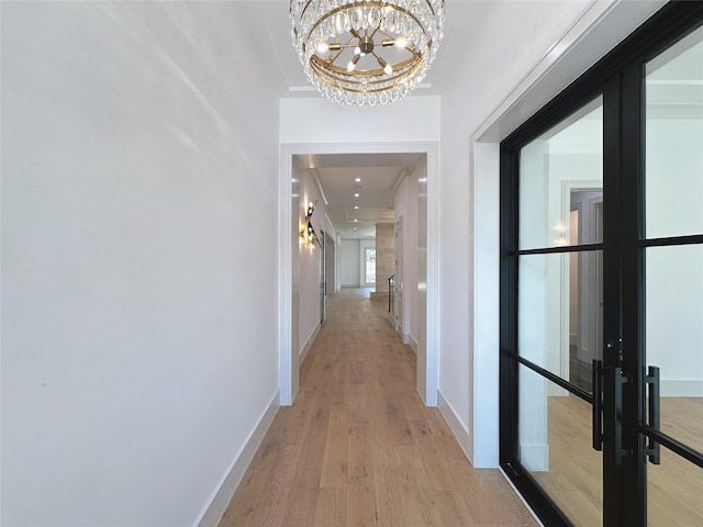 corridor with light wood-type flooring, french doors, and an inviting chandelier