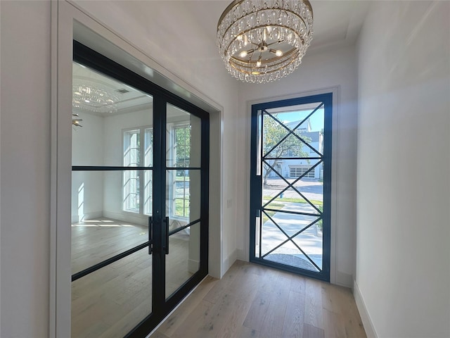 entryway featuring french doors, light hardwood / wood-style flooring, a raised ceiling, and crown molding