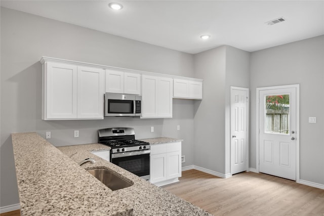 kitchen featuring white cabinetry, sink, light stone counters, light hardwood / wood-style flooring, and appliances with stainless steel finishes