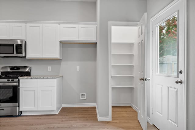 kitchen featuring light stone countertops, white cabinetry, appliances with stainless steel finishes, and light hardwood / wood-style flooring