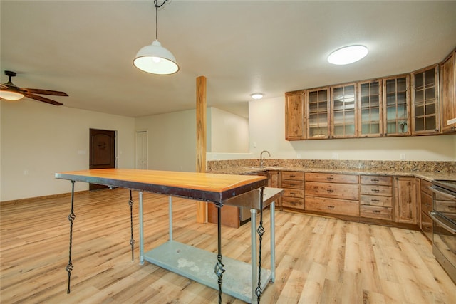 kitchen with light wood-type flooring, double oven range, pendant lighting, ceiling fan, and light stone countertops