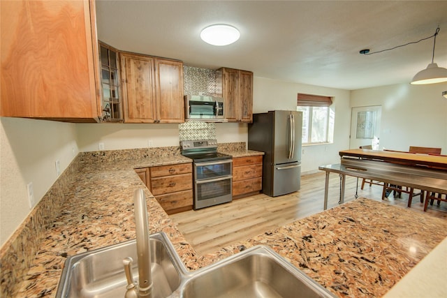 kitchen featuring sink, appliances with stainless steel finishes, light stone countertops, decorative light fixtures, and light wood-type flooring