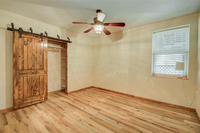 unfurnished bedroom featuring ceiling fan, a barn door, and light hardwood / wood-style floors