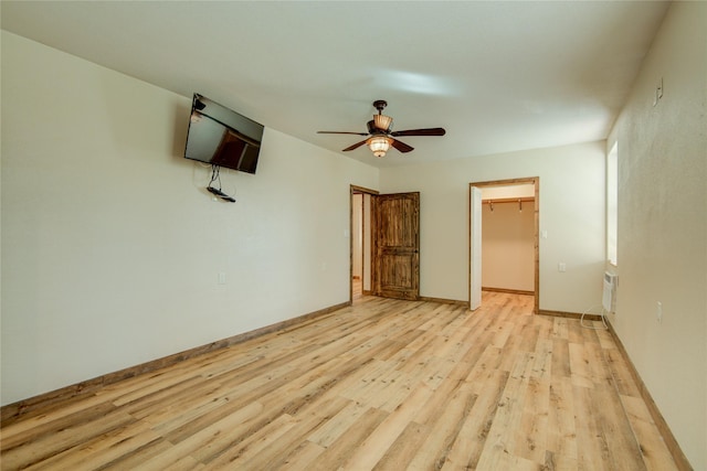 unfurnished bedroom with ceiling fan, a walk in closet, light hardwood / wood-style floors, and a closet