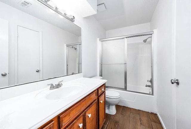 full bathroom featuring toilet, hardwood / wood-style floors, vanity, and combined bath / shower with glass door