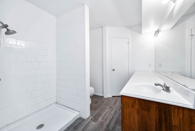 bathroom with hardwood / wood-style flooring, vanity, toilet, and a tile shower