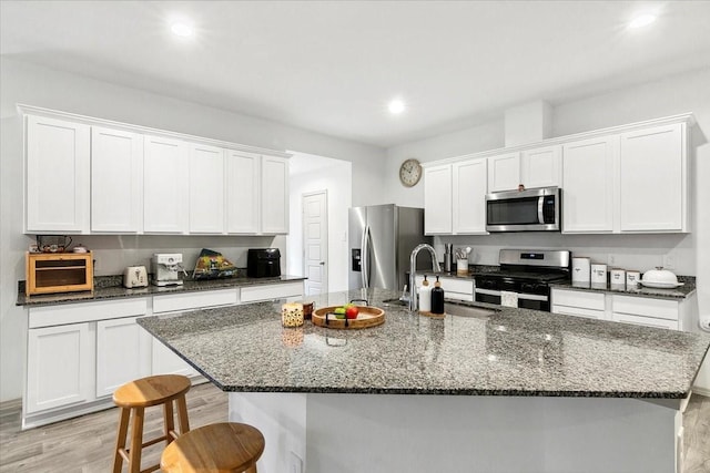 kitchen featuring appliances with stainless steel finishes, light hardwood / wood-style floors, a center island with sink, and sink