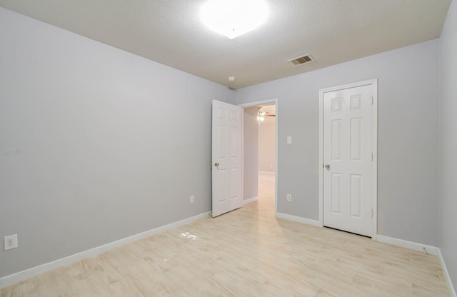 empty room with a textured ceiling and light hardwood / wood-style flooring