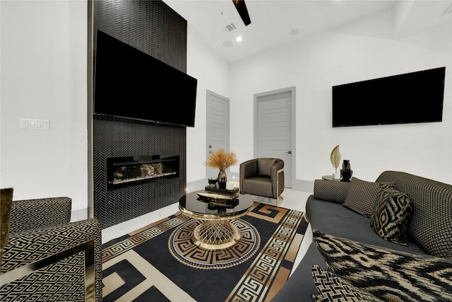 living room featuring tile patterned flooring, a towering ceiling, ceiling fan, and a tiled fireplace