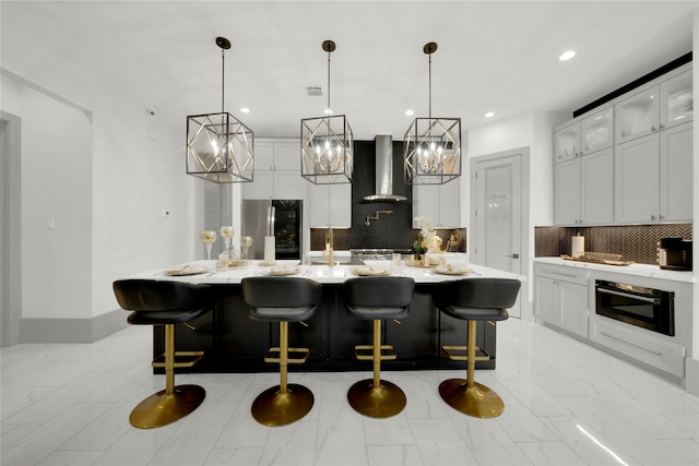 kitchen with pendant lighting, backsplash, a large island with sink, wall chimney exhaust hood, and appliances with stainless steel finishes