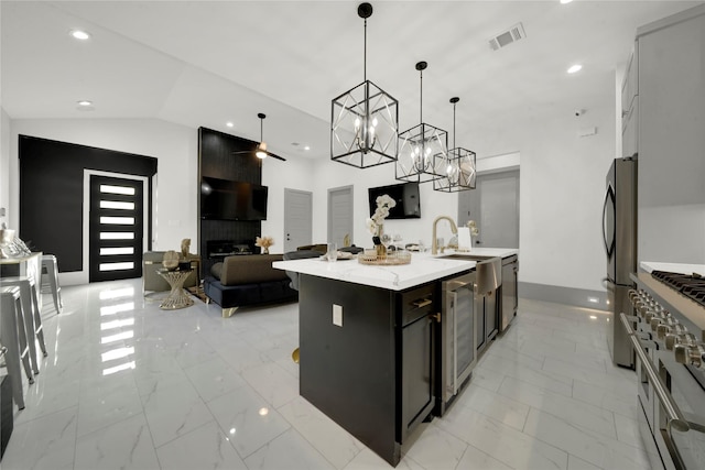 kitchen with a kitchen island with sink, ceiling fan with notable chandelier, hanging light fixtures, vaulted ceiling, and appliances with stainless steel finishes