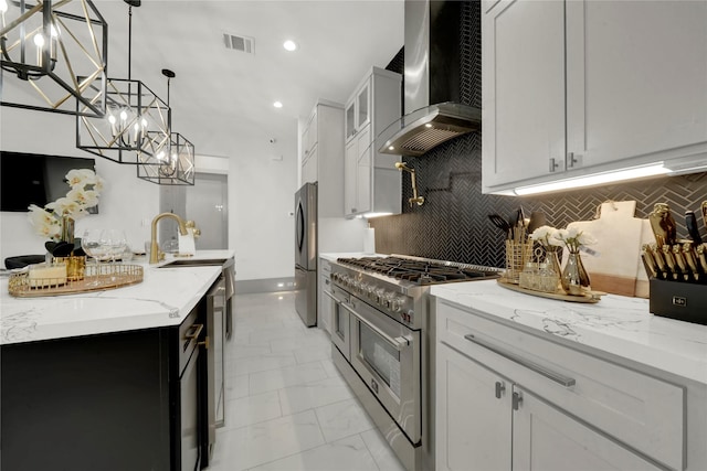 kitchen with white cabinets, wall chimney exhaust hood, pendant lighting, and appliances with stainless steel finishes