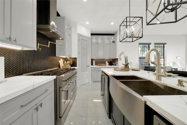 kitchen with tasteful backsplash, high end stainless steel range oven, wall chimney range hood, white cabinets, and hanging light fixtures