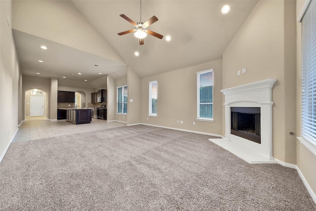 unfurnished living room featuring ceiling fan, high vaulted ceiling, and light carpet