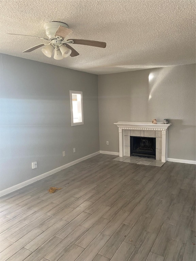 unfurnished living room featuring ceiling fan, wood-type flooring, a textured ceiling, and a tiled fireplace