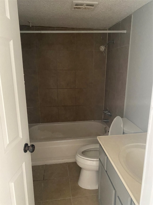 full bathroom with tile patterned flooring, tiled shower / bath combo, toilet, and a textured ceiling