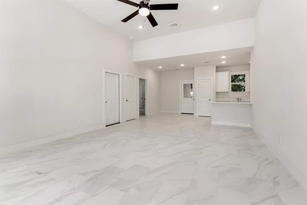 unfurnished living room featuring ceiling fan and a high ceiling