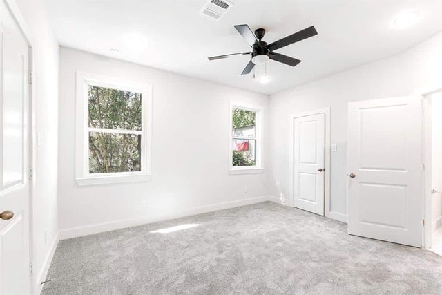 unfurnished bedroom featuring multiple windows, light colored carpet, and ceiling fan