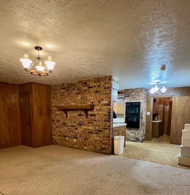 unfurnished living room with a textured ceiling, light colored carpet, an inviting chandelier, and wooden walls