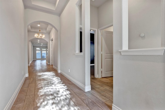 corridor with a tray ceiling and a chandelier