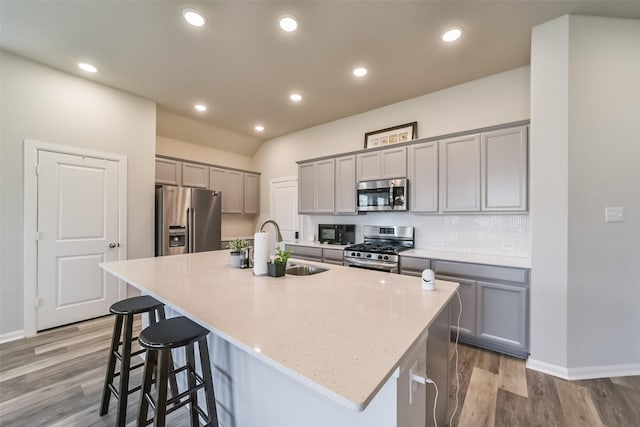 kitchen featuring appliances with stainless steel finishes, light stone counters, sink, a center island with sink, and light hardwood / wood-style flooring