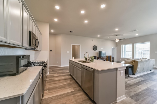 kitchen featuring gray cabinetry, sink, an island with sink, light hardwood / wood-style floors, and appliances with stainless steel finishes