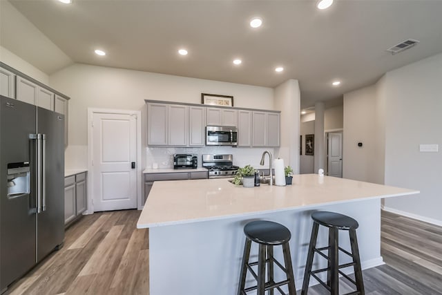 kitchen with a center island with sink, gray cabinetry, light wood-type flooring, and stainless steel appliances