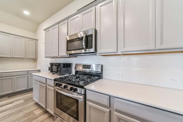 kitchen with backsplash, gray cabinets, light wood-type flooring, and appliances with stainless steel finishes