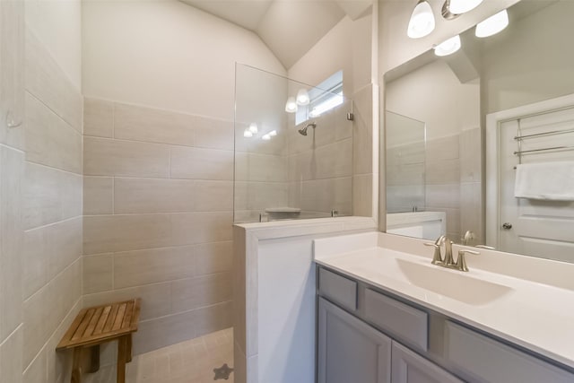 bathroom featuring a tile shower, tile walls, vanity, and lofted ceiling